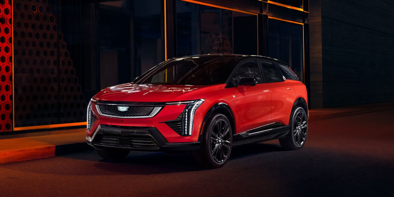 A bright red 2025 Cadillac OPTIQ SUV with sleek lines parked under a modern building at night.